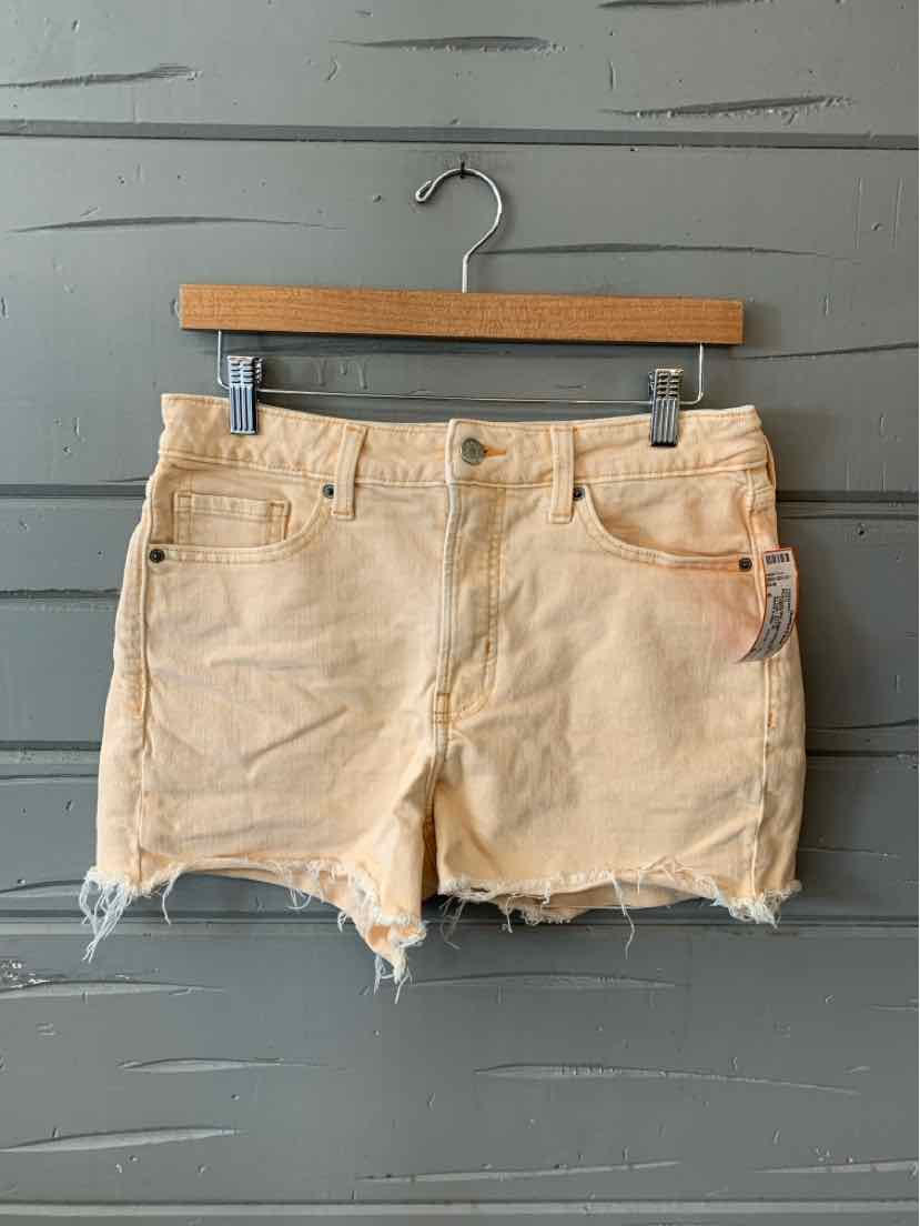 Light beige distressed denim shorts with frayed hems and front pockets hanging on wooden hanger.