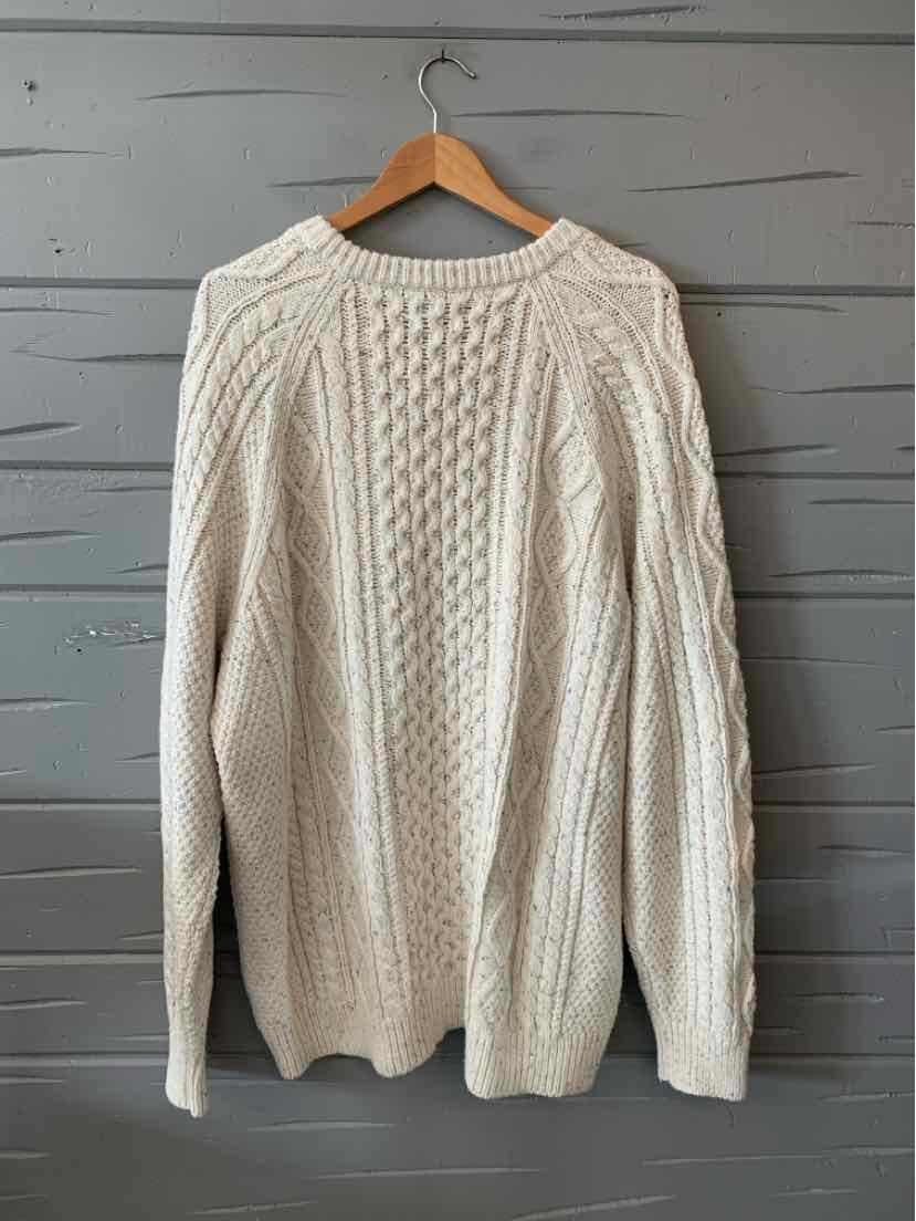 Oatmeal-colored cable knit sweater with long sleeves and crew neckline hanging on wooden hanger.