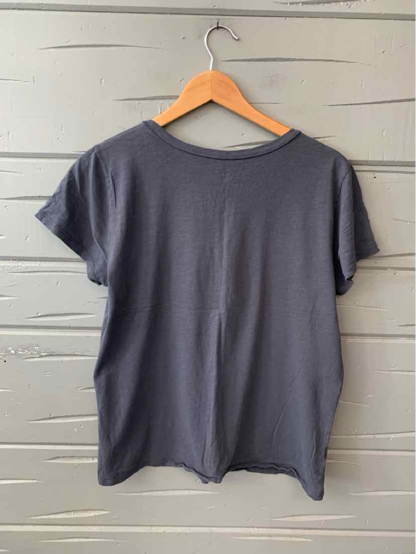 Gray short-sleeve cotton t-shirt with crew neck, hanging on wooden hanger against gray wooden wall.