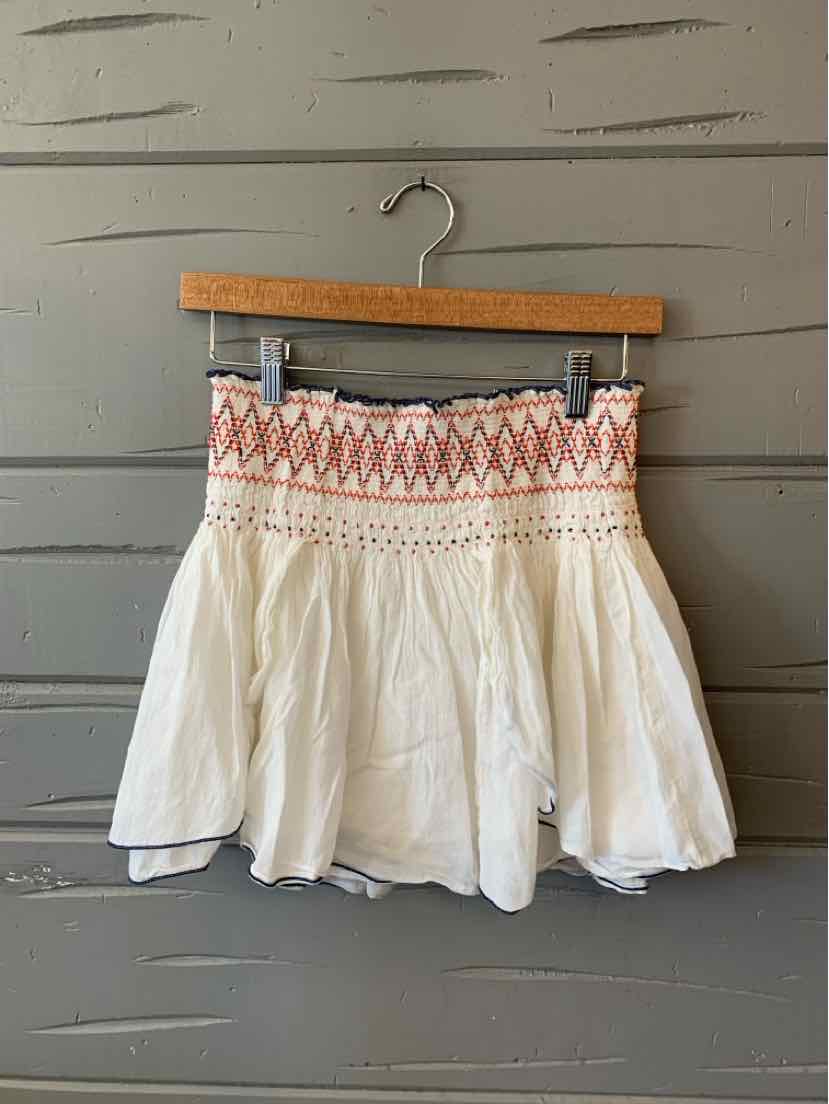White flowy mini skirt with smocked waist and orange geometric embroidery trim.