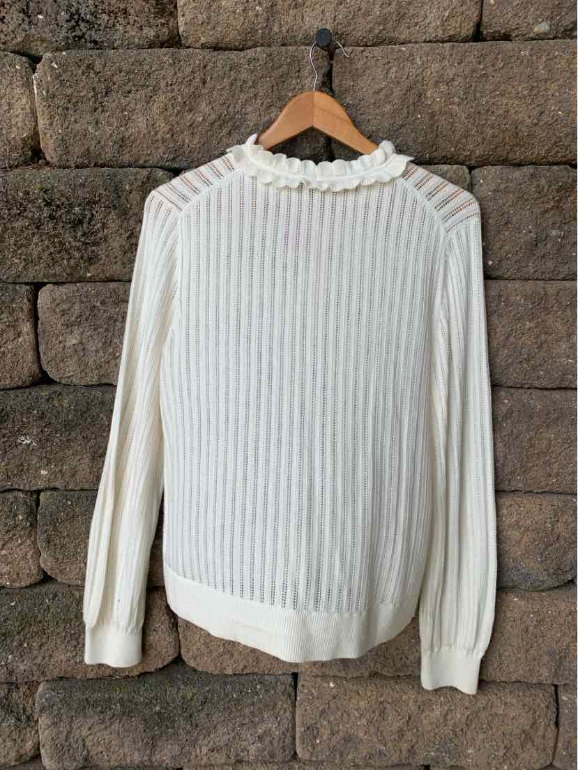Cream-colored ribbed knit sweater with ruffled collar and long sleeves on wooden hanger.
