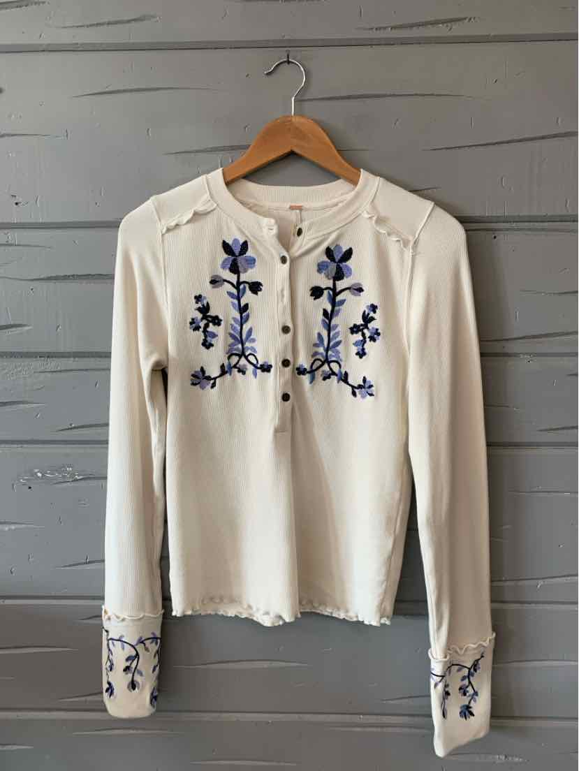 Cream long-sleeve top with blue floral embroidery on chest and cuffs, scalloped edges.