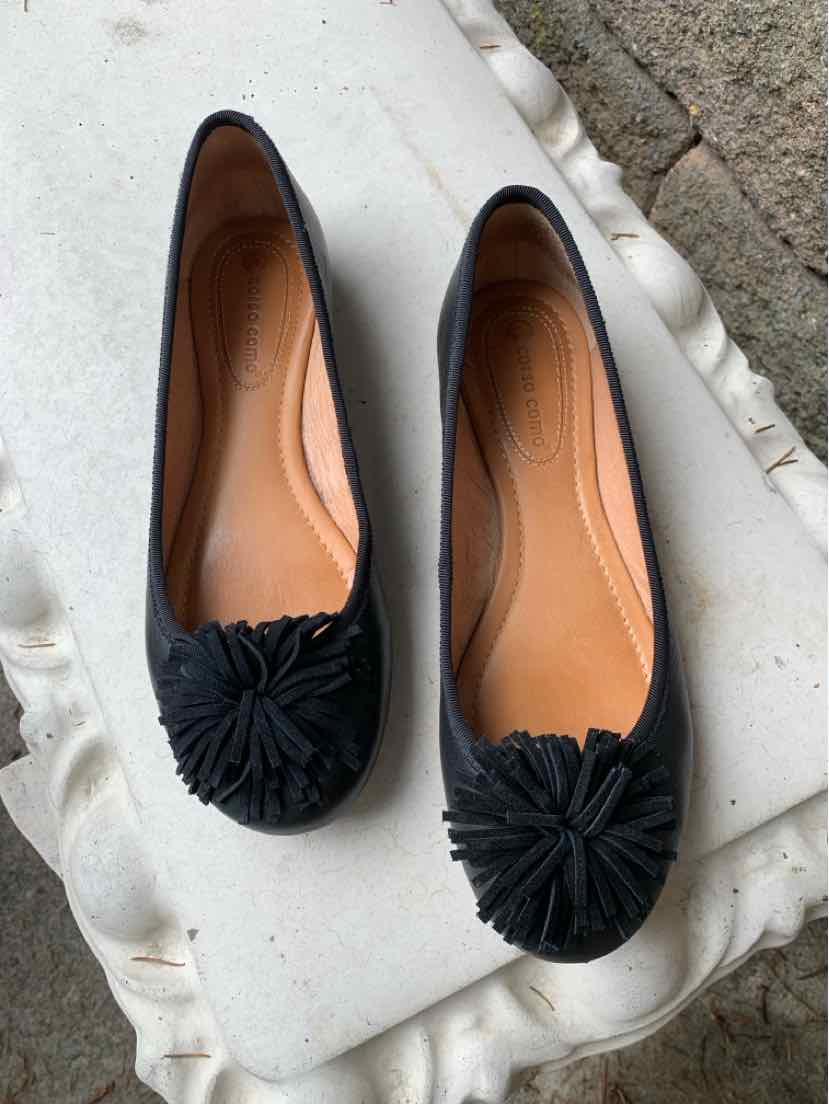 Black ballet flats with rounded toes and fabric floral embellishments on top, tan insoles.