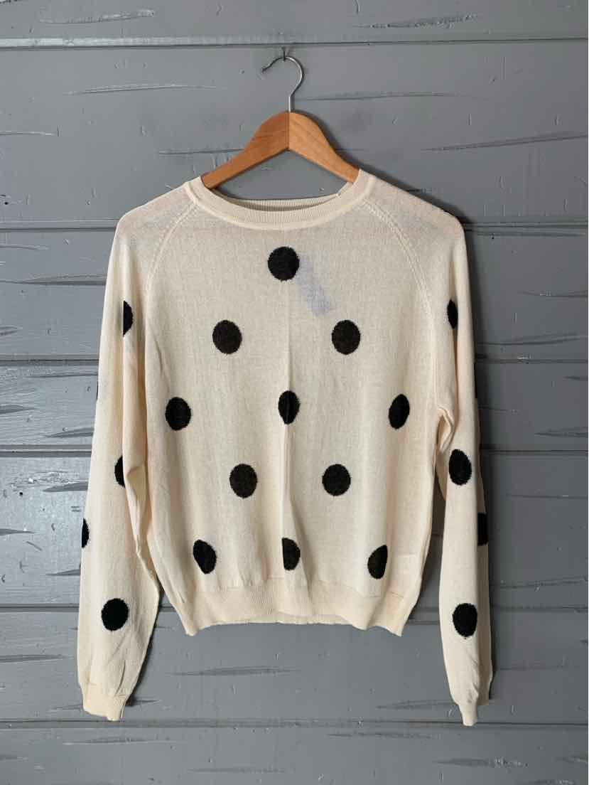 Cream knit sweater with large black polka dots, ribbed neckline, cuffs, and hem, hanging on a wooden hanger.