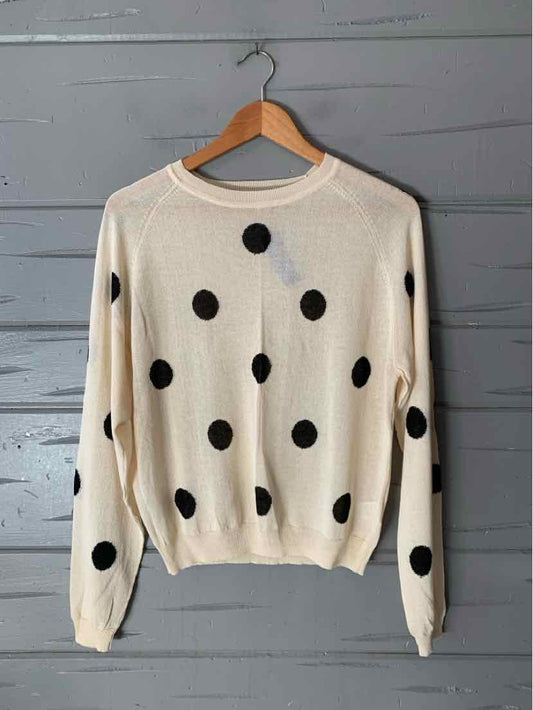 Cream knit sweater with large black polka dots, ribbed neckline, cuffs, and hem, hanging on a wooden hanger.