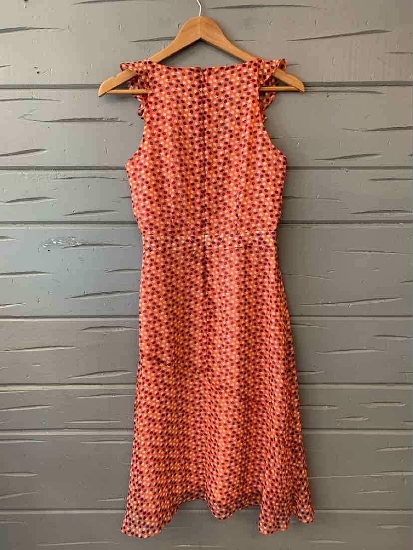 Orange sleeveless dress with white and black geometric dot pattern, fitted waist, and knee-length hem on wooden hanger.