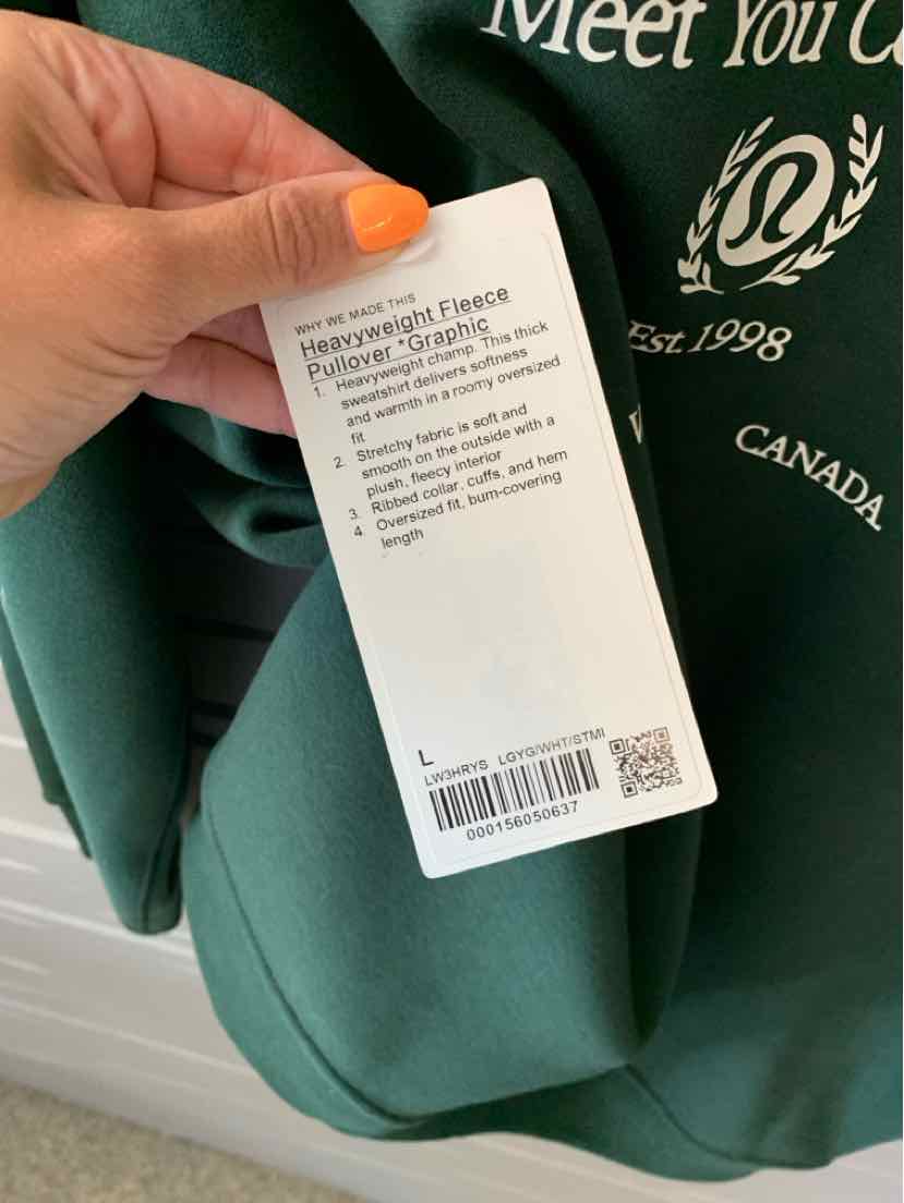Green Lululemon sweatshirt tag held by hand, showing product details and barcode.