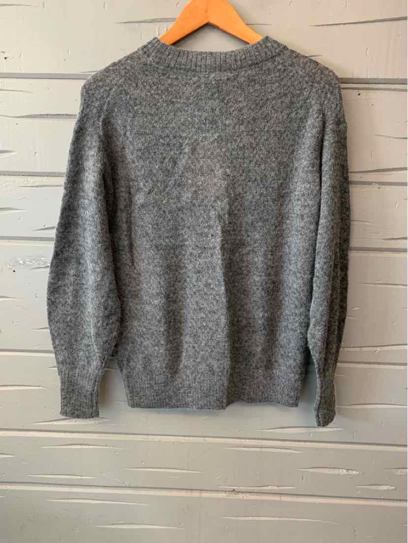 Gray knit sweater with long sleeves and a crew neckline hanging on a wooden hanger.