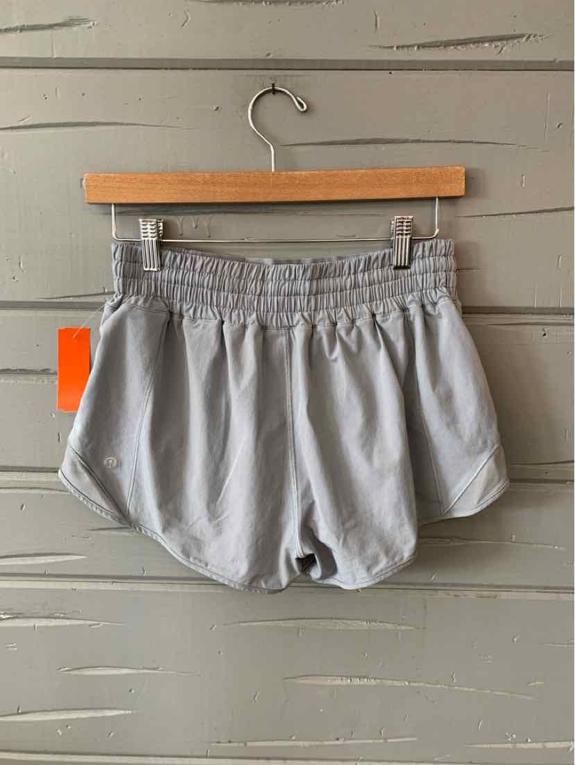 Light gray athletic shorts with elastic waistband and curved hem detail hanging on wooden hanger.