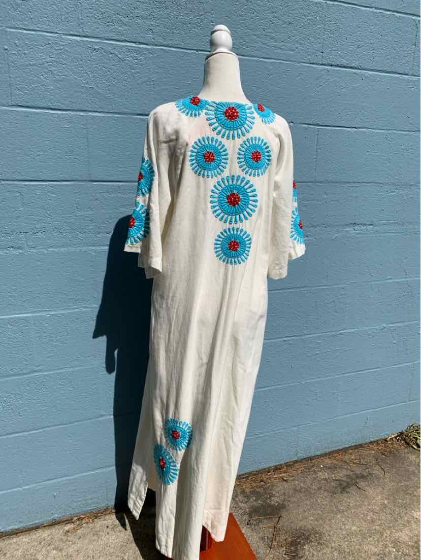 White maxi dress with blue and red circular embroidery, elbow-length sleeves, and side slits.