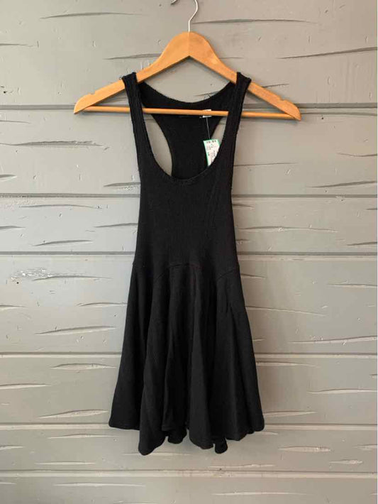 Black sleeveless mini dress with flared skirt hanging on wooden hanger against gray wall.