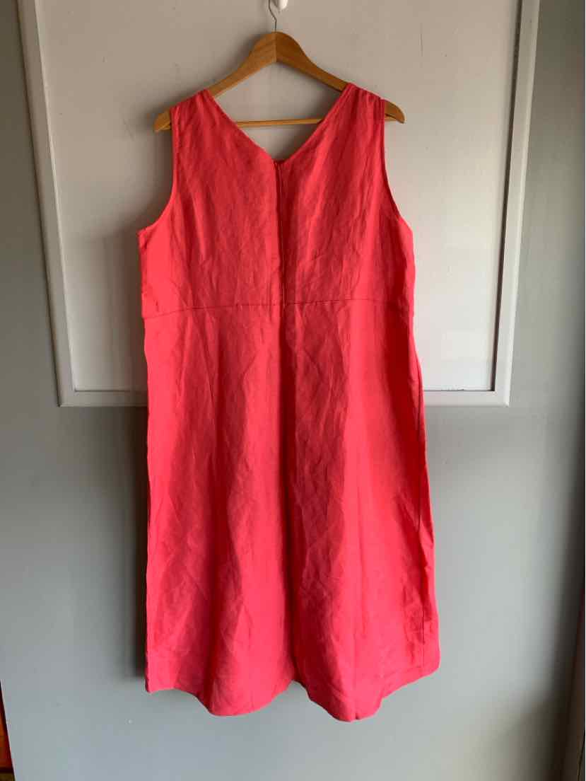 Sleeveless bright pink linen dress with V-neck and loose fit hanging on wooden hanger.