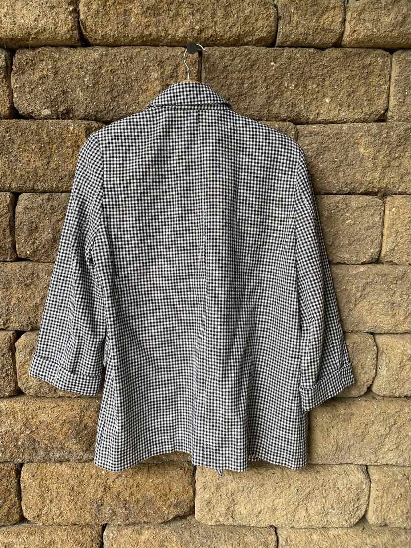 Black and white small gingham blazer with long sleeves and notched collar hanging on stone wall.
