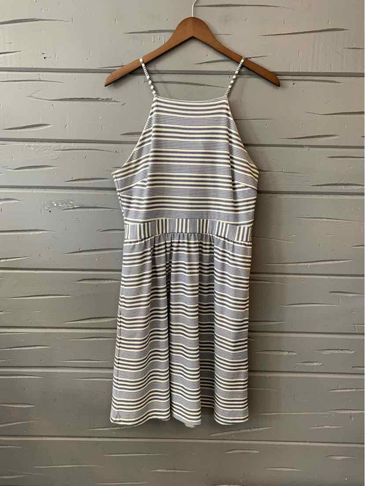 Sleeveless white dress with thin brown and yellow horizontal stripes and gathered waist hanging on wooden hanger.