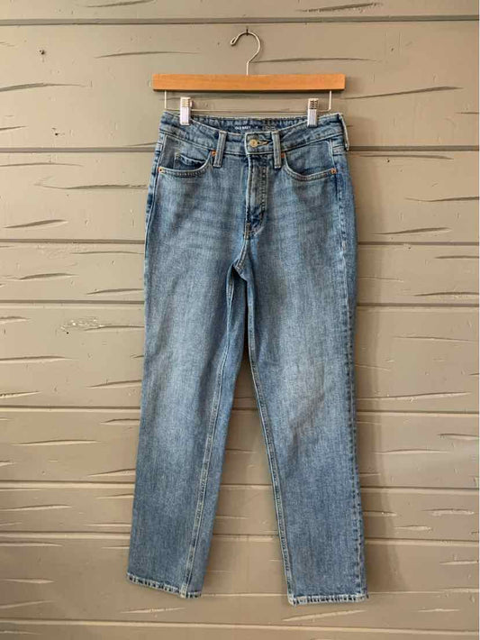 Light blue straight-leg denim jeans with classic five-pocket design hanging on wooden hanger against beige wooden background.