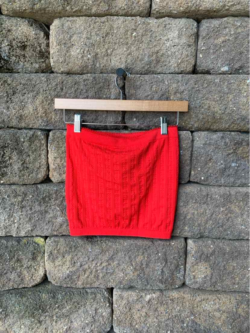 Bright red knitted mini skirt with cable-knit pattern, elastic waistband, and fitted shape hanging on wooden hanger.
