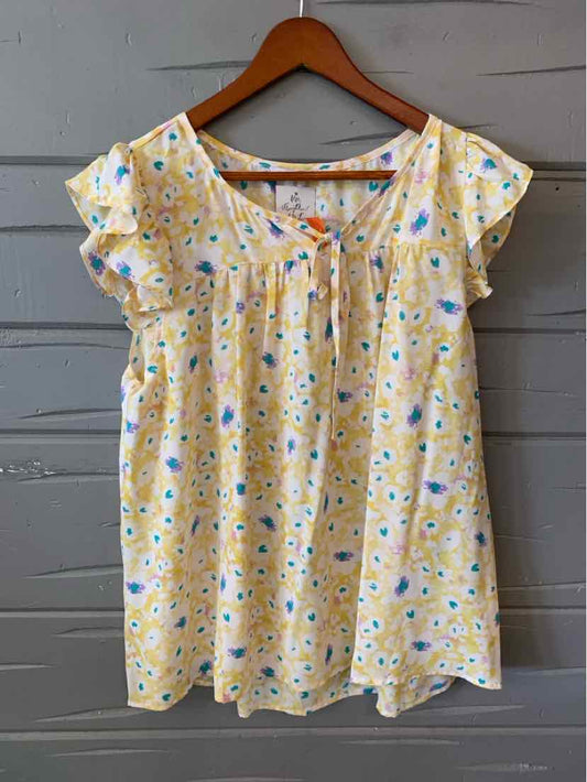 Light yellow floral blouse with short flutter sleeves and a square neckline on wooden hanger.