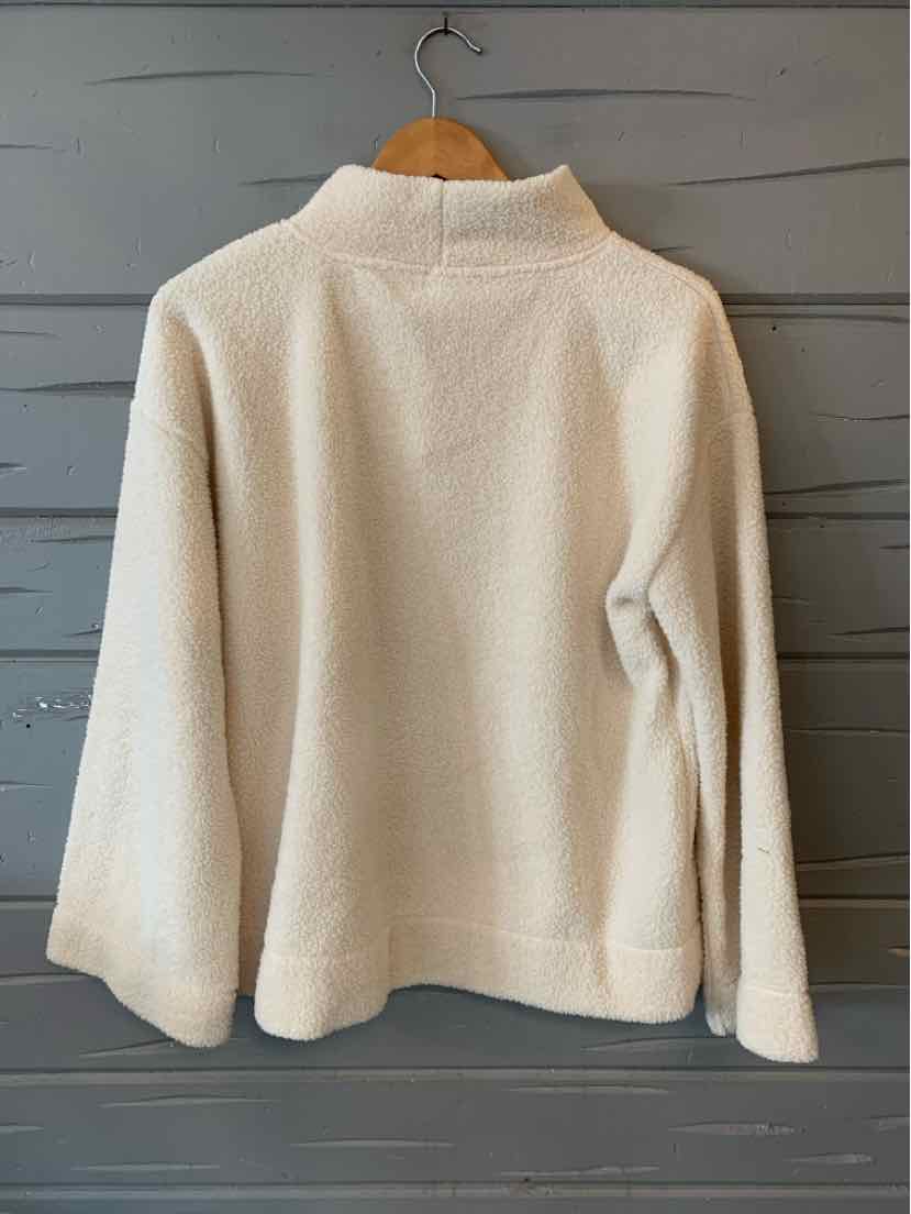 Cream-colored sherpa fleece jacket with a high collar and relaxed fit hanging on wooden hanger.