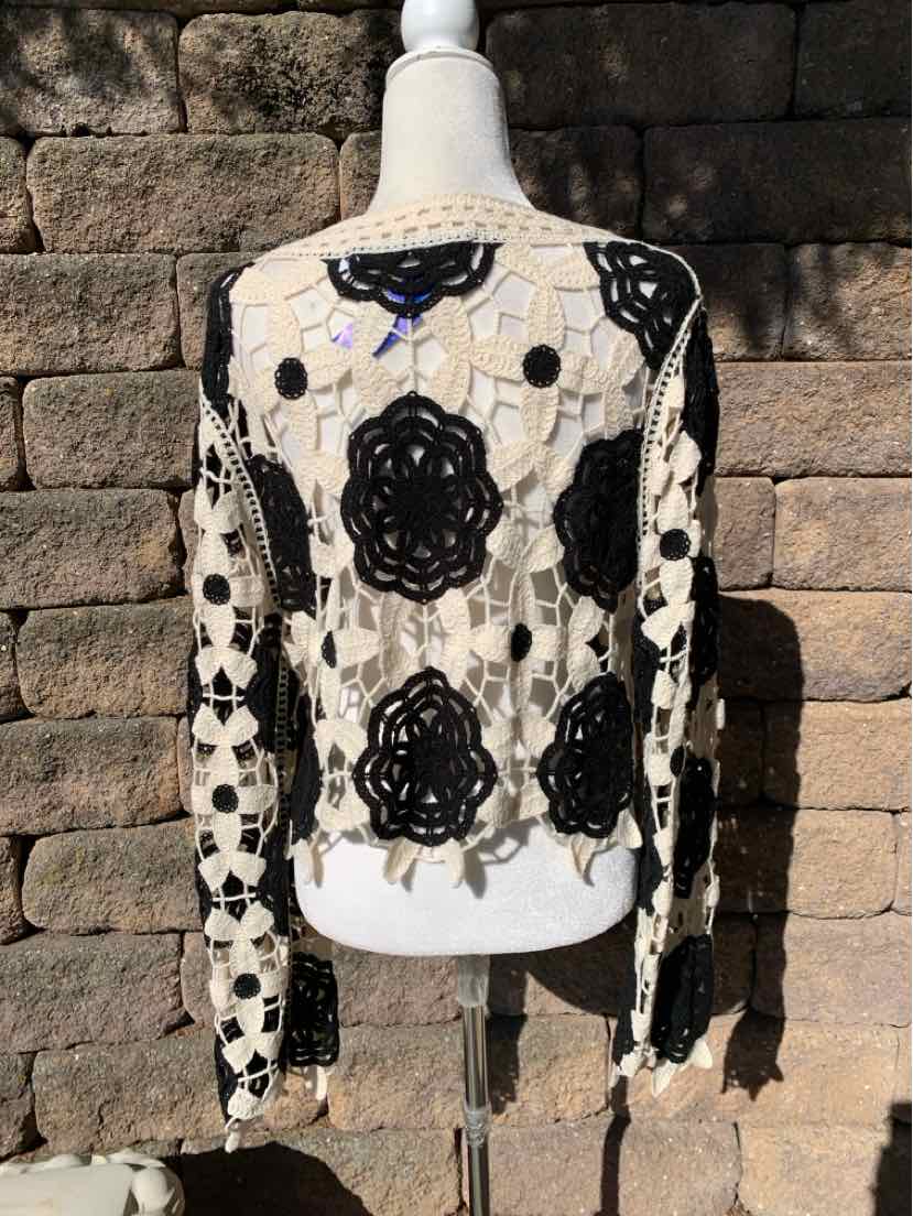 Black floral lace cardigan with sheer sleeves and large appliqué flowers on a white mannequin.