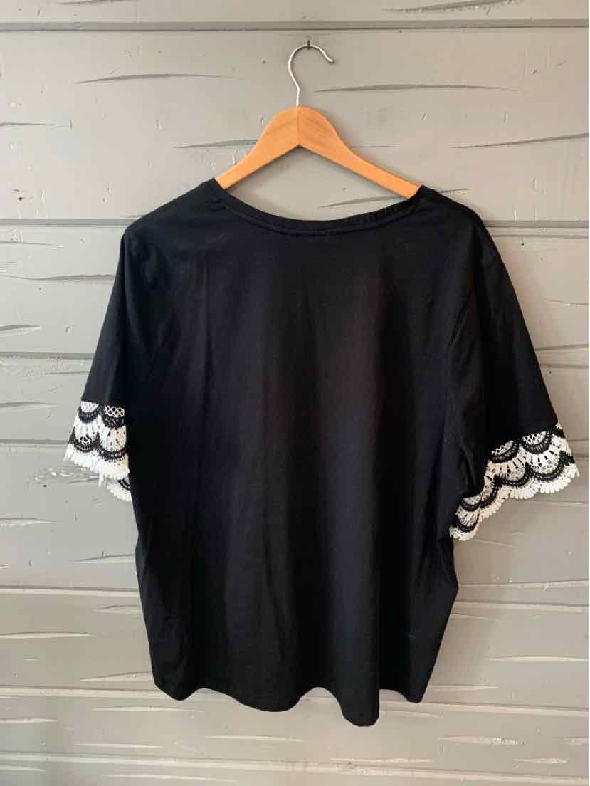 Black blouse with wide sleeves featuring white lace scalloped trim, hanging on wooden hanger.