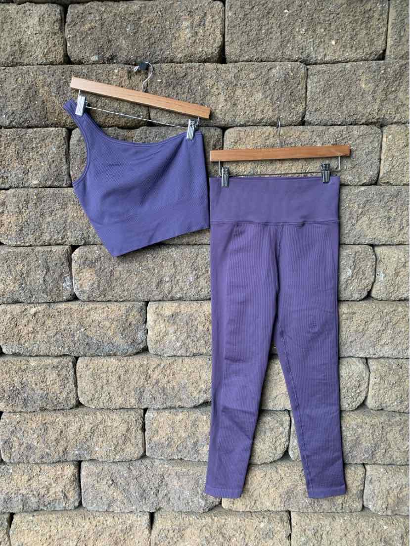 Purple seamless sports bra and high-waist leggings set hanging against a stone wall.