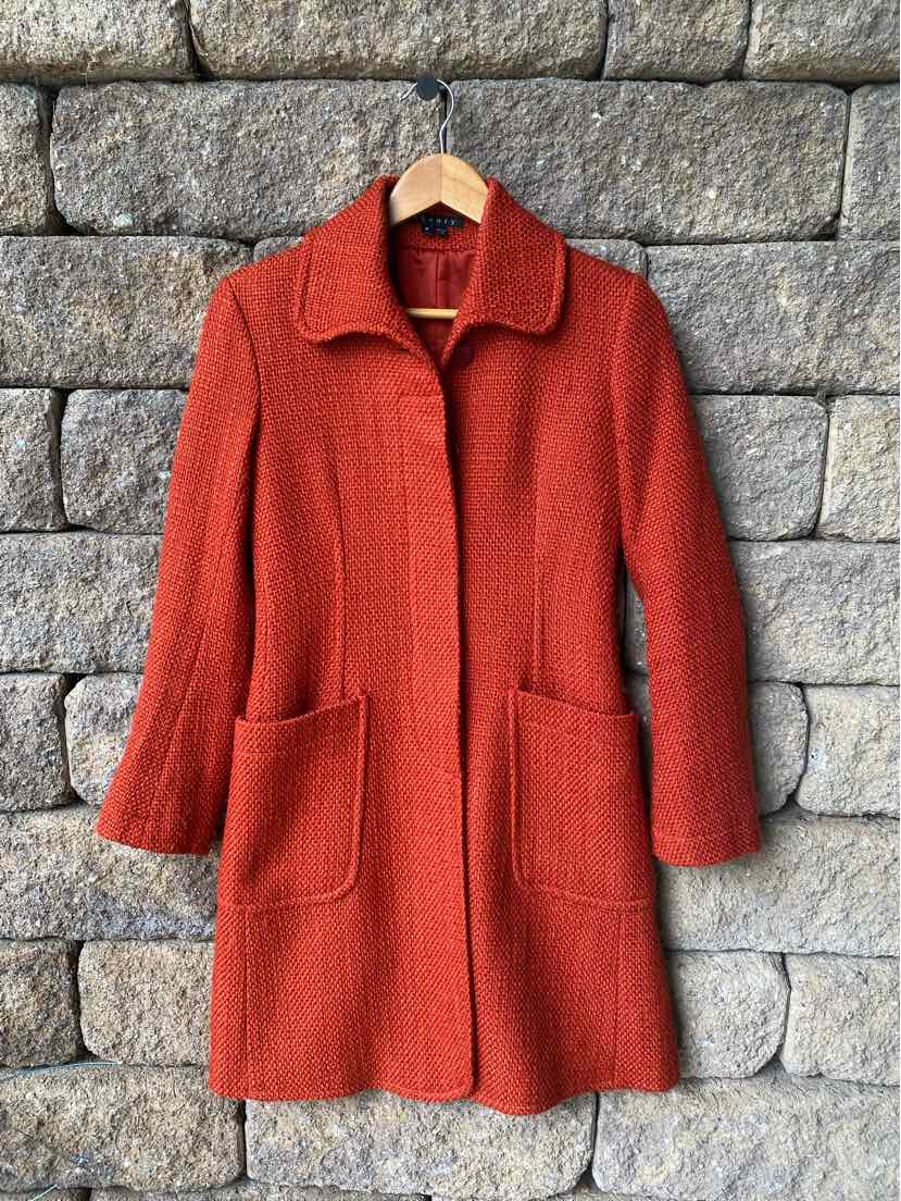 Rust-orange wool coat with a straight fit, large front patch pockets, and a classic collar hanging on a wooden hanger.