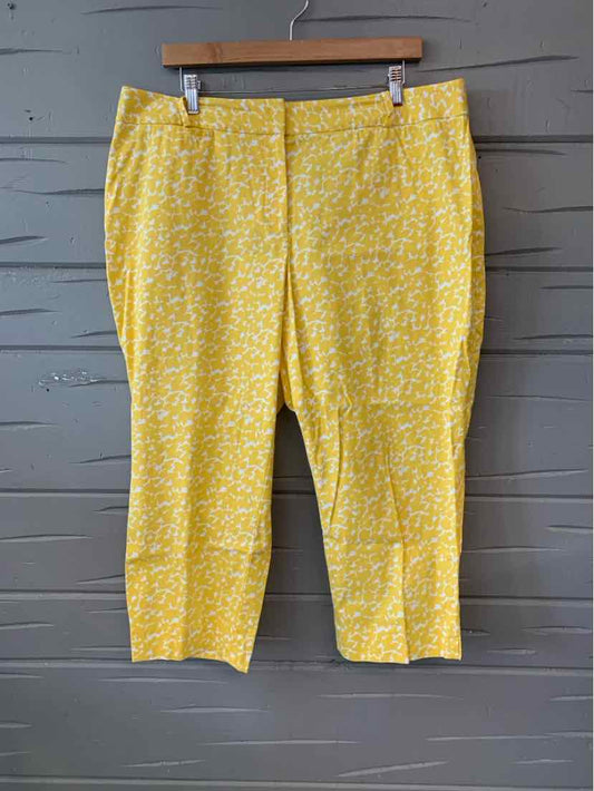 Yellow cropped pants with white floral pattern and front pockets hanging on wooden hanger.