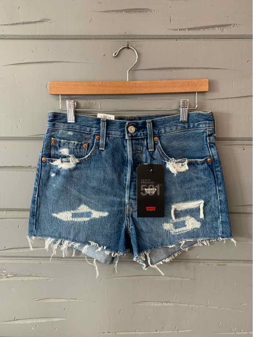 Blue distressed denim shorts with frayed hems and front pockets hanging on wooden hanger.