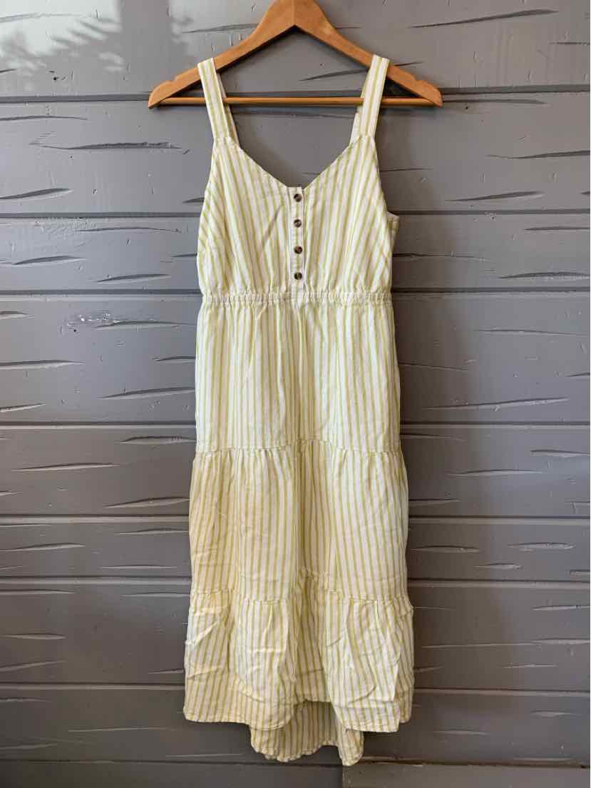 Green and white vertical striped sleeveless dress with button-down front and tiered hem hanging on wooden hanger.