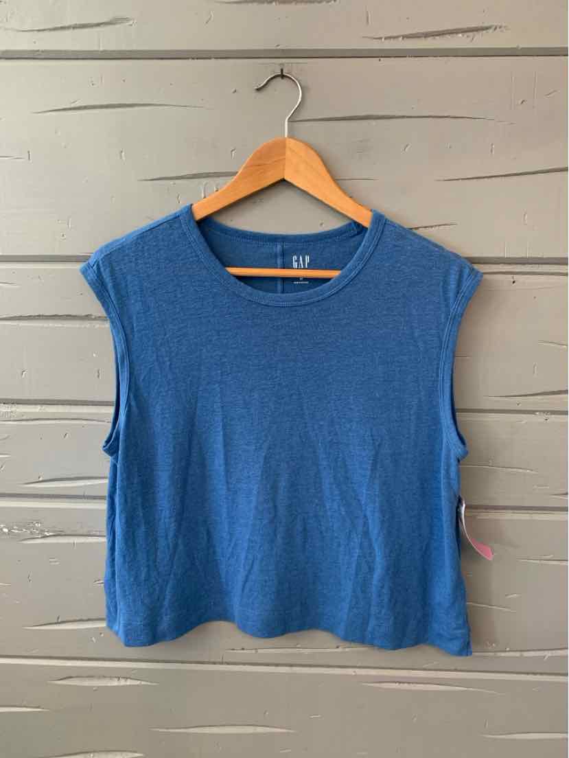 Blue sleeveless crew neck top with relaxed fit hanging on wooden hanger against gray wall.