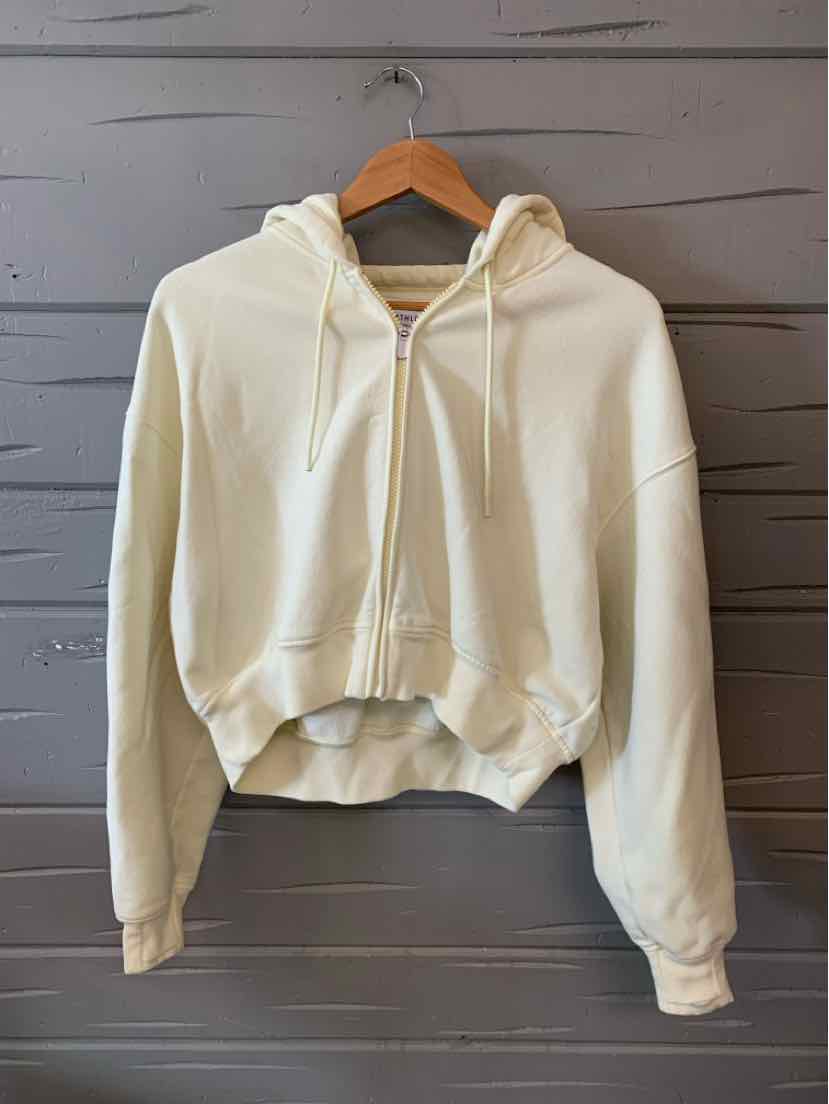 Cream-colored cropped hoodie with long sleeves, front kangaroo pocket, and adjustable drawstring hood.