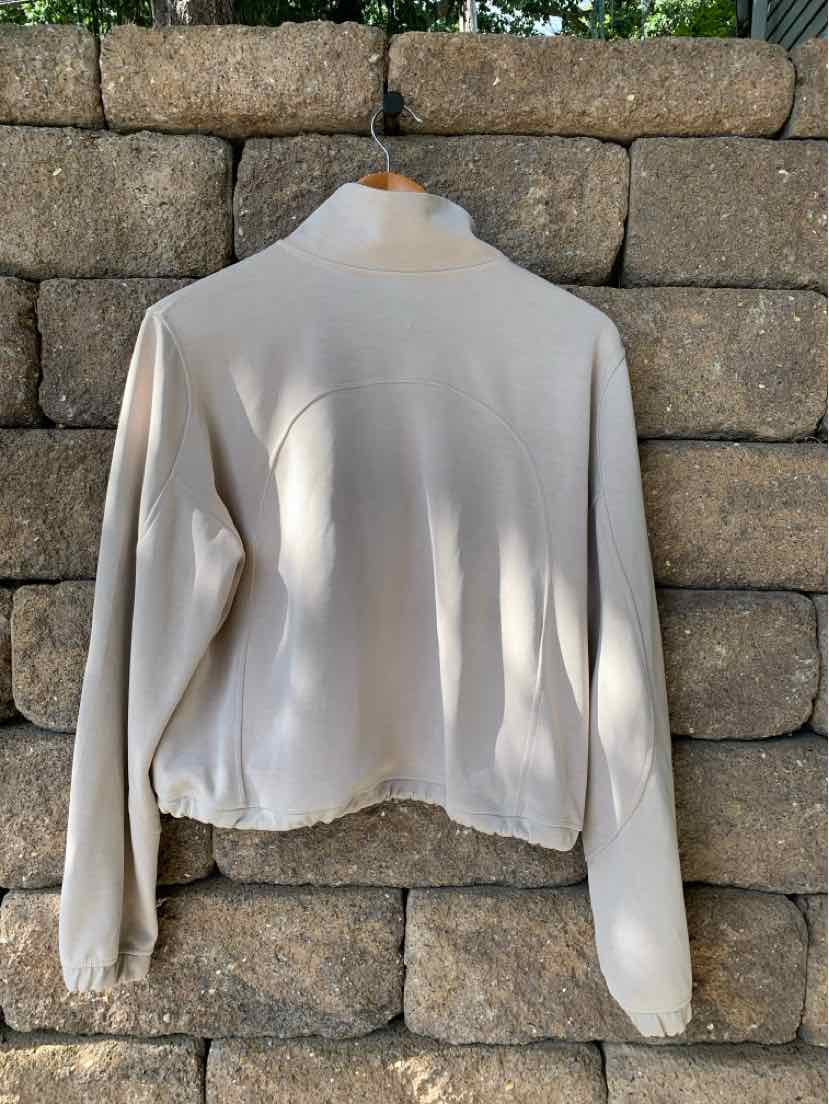 Tan long-sleeve lightweight jacket with a collar and slightly gathered hem hanging on a wooden hanger.