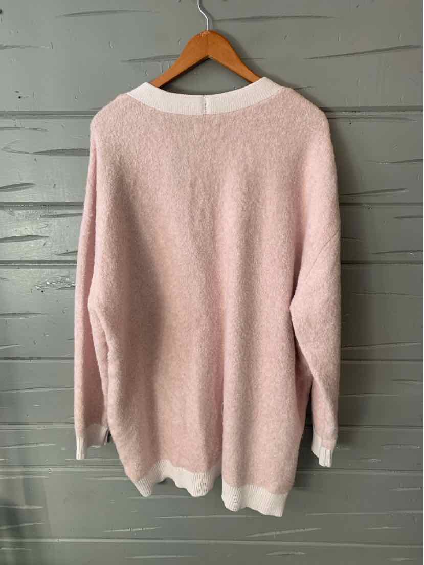 Pastel pink oversized sweater with white ribbed crew neck, cuffs, and hem on wooden hanger.