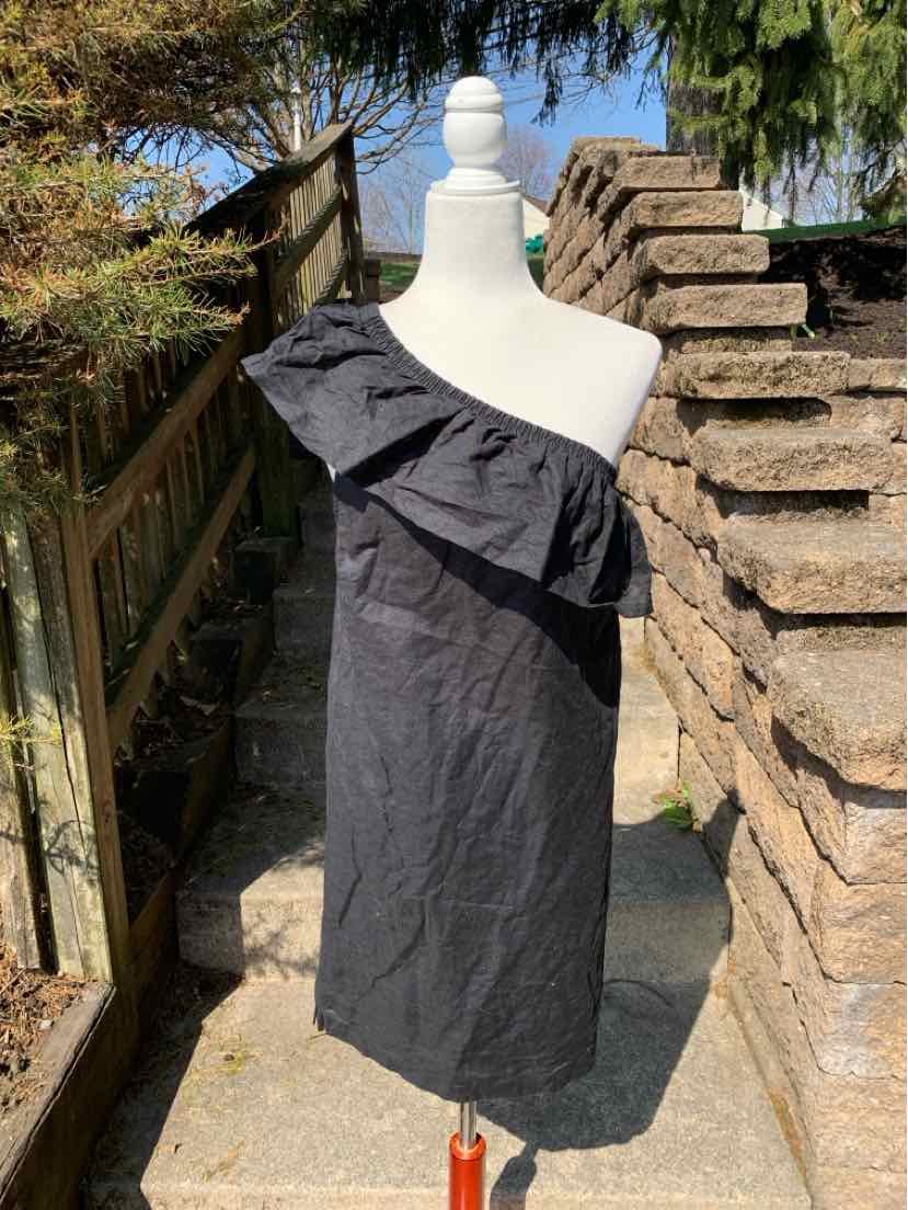 Black one-shoulder dress with ruffle detail and knee-length hem on mannequin outdoors.