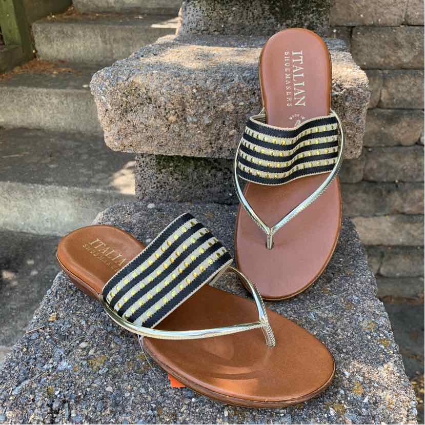 Brown leather sole sandals with black and cream striped fabric strap and thin metallic thong design.