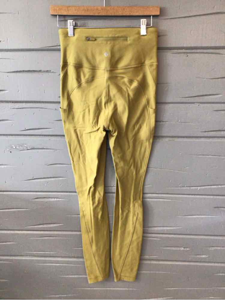 Olive green high-waisted Lululemon leggings with seam details hanging on wooden hanger against gray wall.