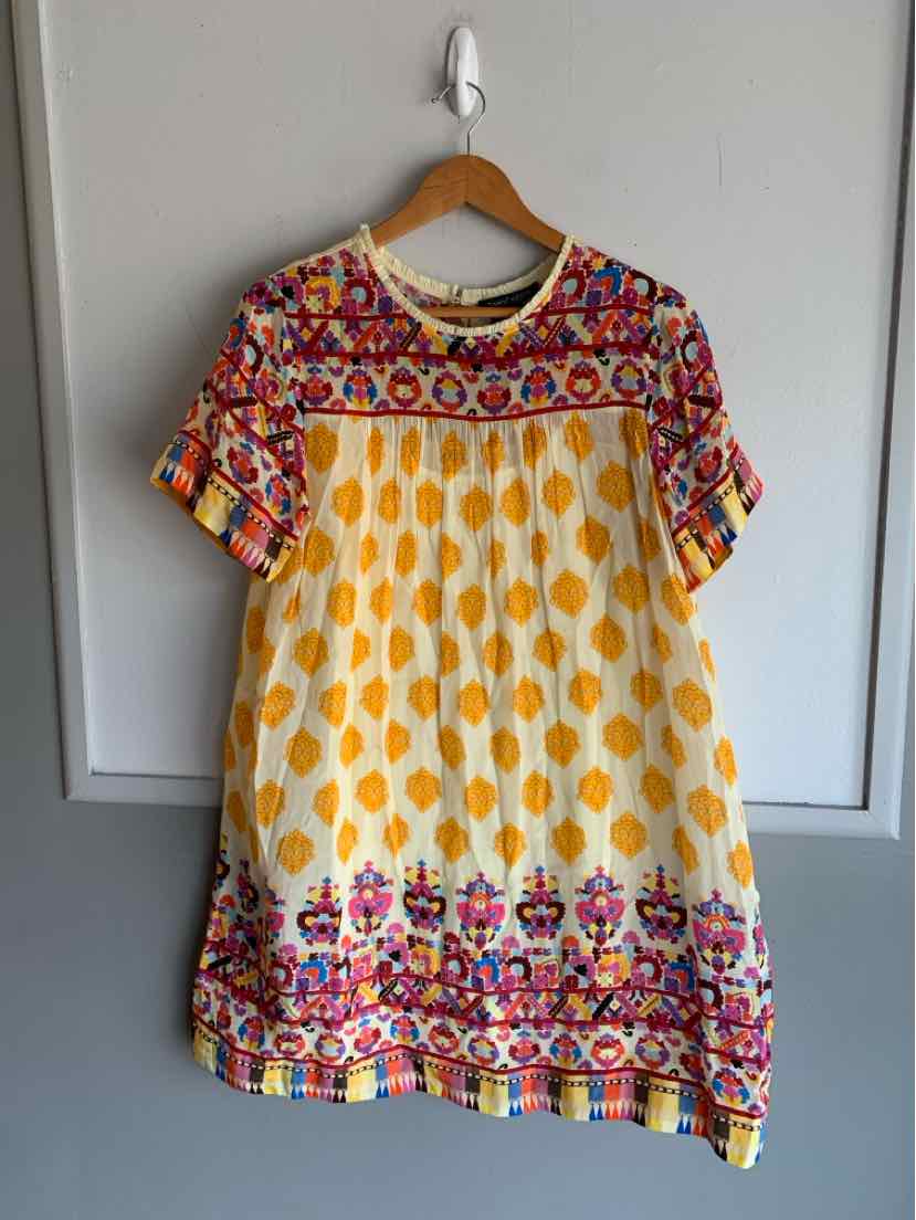 Short-sleeve tunic dress with yellow floral patterns, multicolor embroidered neckline, and hem detailing.