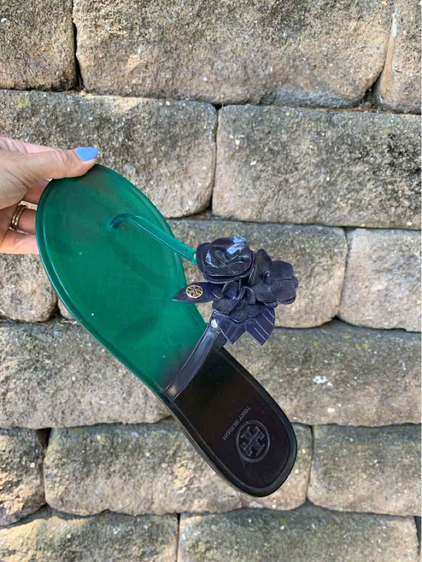Black flat sandal with green footbed, featuring a fabric flower embellishment on the strap and a Tory Burch logo on the sole.