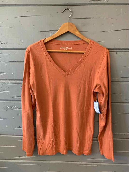 Coral-orange Eddie Bauer women’s long-sleeve top with a V-neck and soft knit fabric, hanging on a wooden hanger.