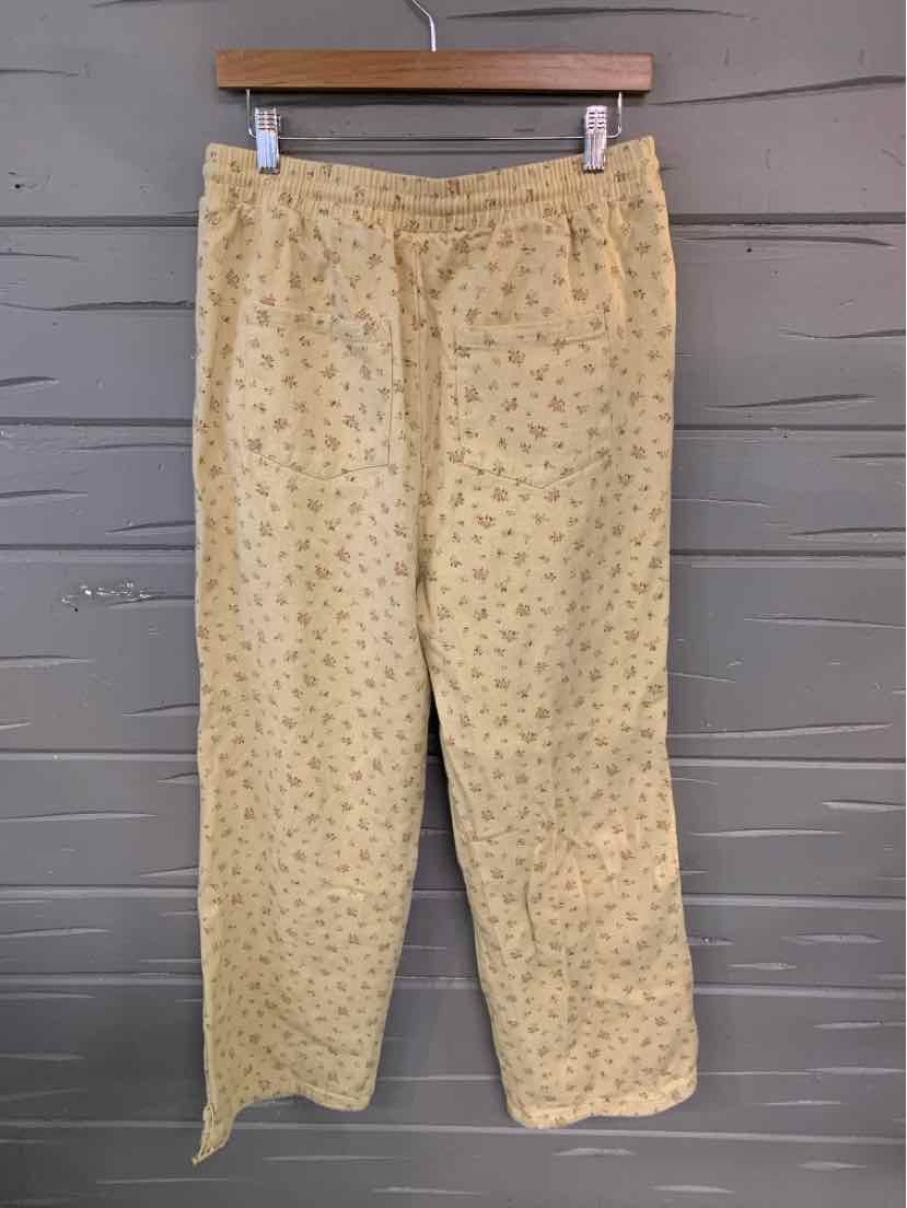 Beige pants with small floral print, straight leg cut, and elastic waistband hanging on wooden hanger.