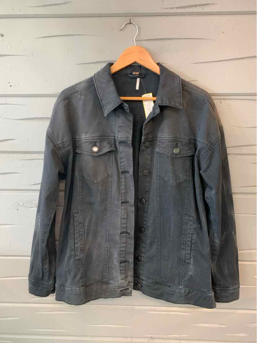 Black denim jacket with button front and flap chest pockets hanging on wooden hanger.