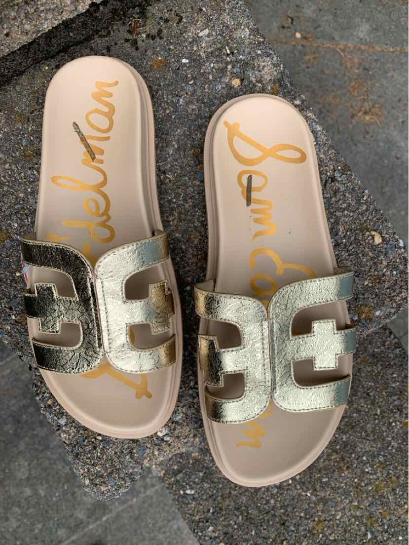 Metallic gold slide sandals with cutout strap design and beige cushioned soles.