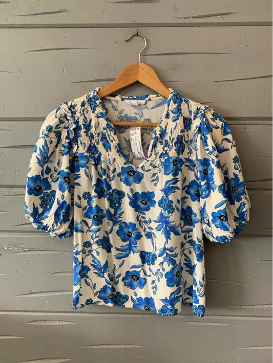 White short-sleeve blouse with blue floral print and gathered neckline on wooden hanger.
