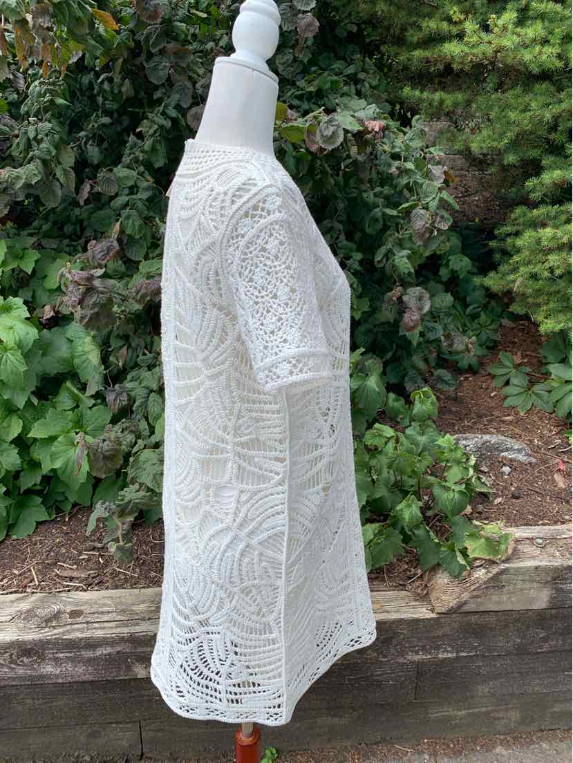 White crochet lace blouse with intricate floral patterns and three-quarter sleeves on mannequin.