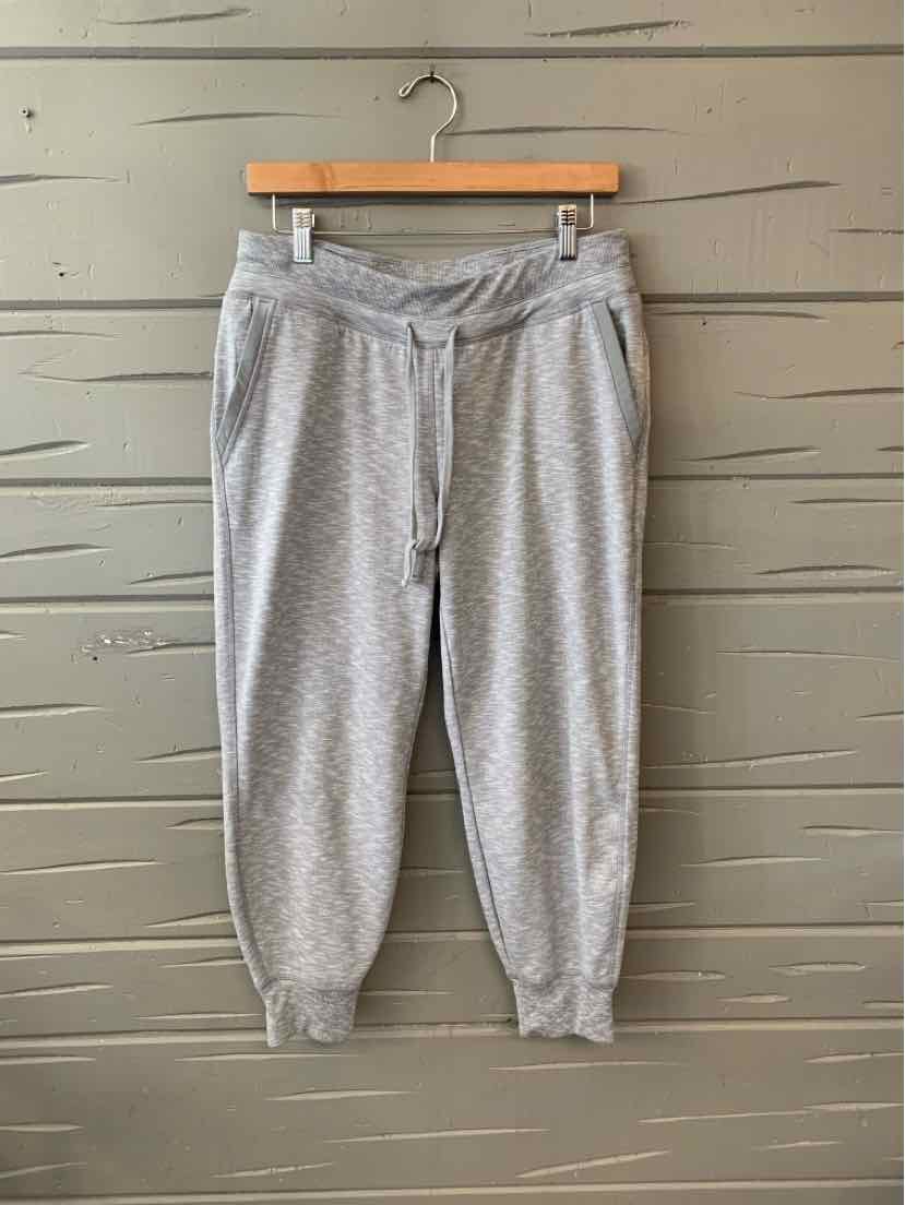 Light gray small-sized sweatpants with elastic waistband, drawstring, and cuffed ankles hanging on wooden hanger.