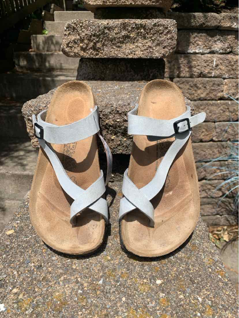 Gray leather sandals with crisscross straps and adjustable black buckles on a contoured cork footbed.