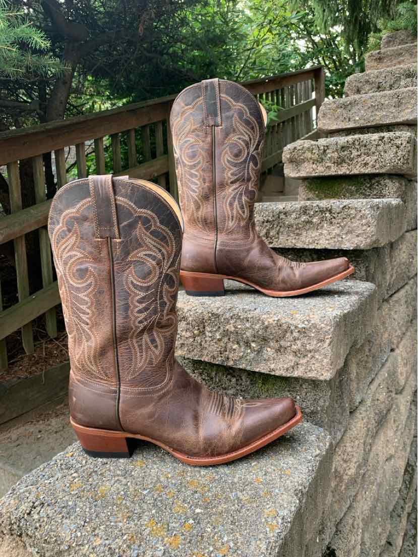 Brown leather western boots with decorative stitching, pointed toes, and stacked heels placed on outdoor stone steps.