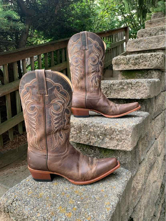 Brown leather western boots with decorative stitching, pointed toes, and stacked heels placed on outdoor stone steps.
