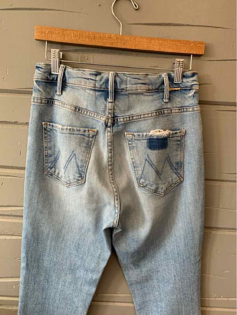 Light wash blue denim jeans with distressed back right pocket and classic five-pocket design hanging on wooden hanger.