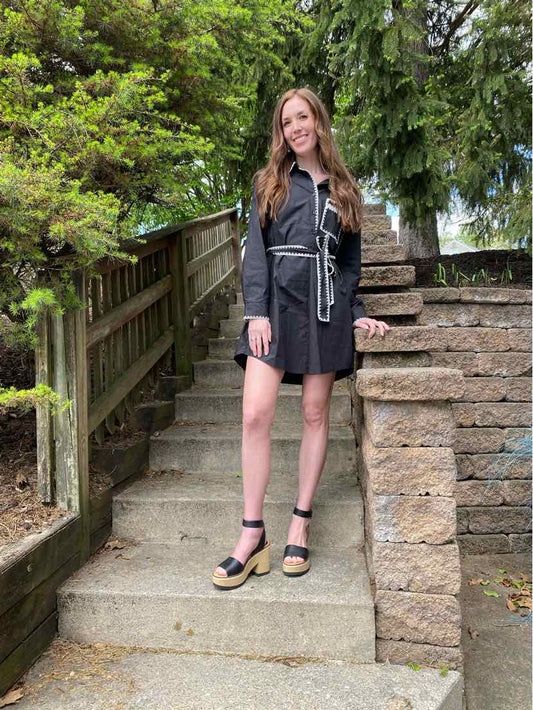 Black long-sleeve mini dress with a wrap-style belt, cinched waist, worn with black platform sandals.